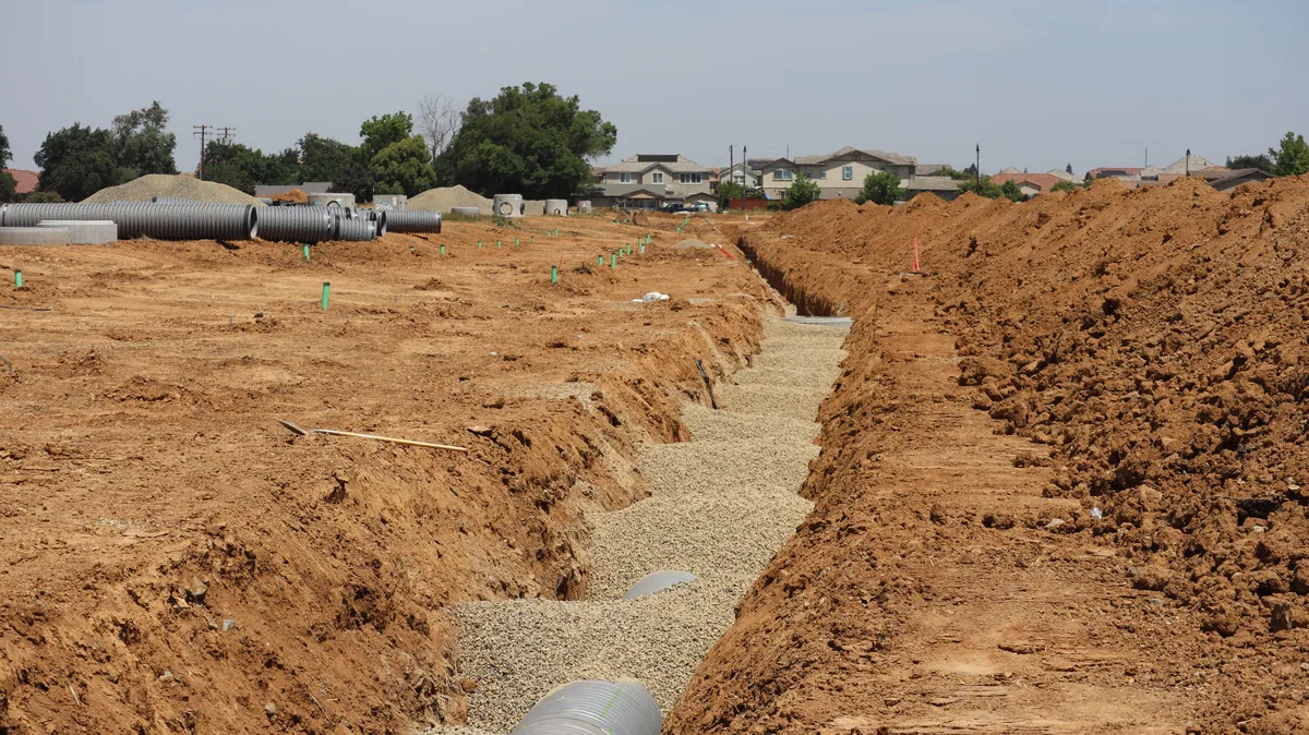 Open excavated trench with gravel bedding and pipe at a residential development site